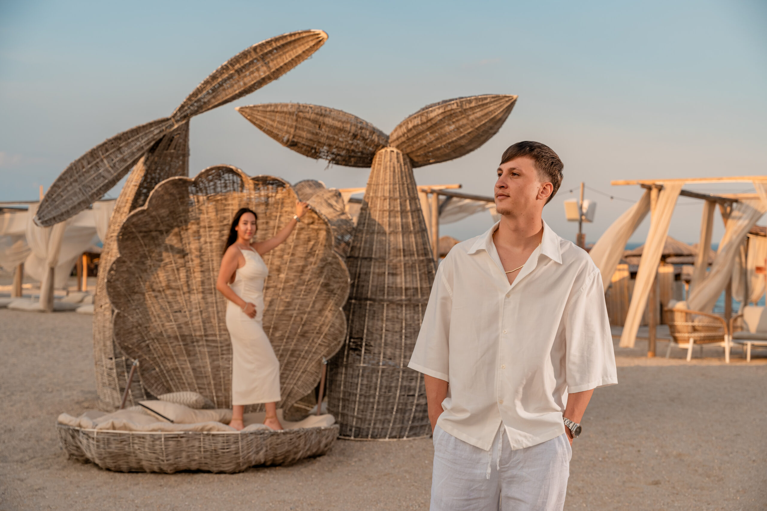 Cuplu într-o ședință foto pre-wedding pe plajă, într-un decor artistic cu elemente sculpturale din ratan