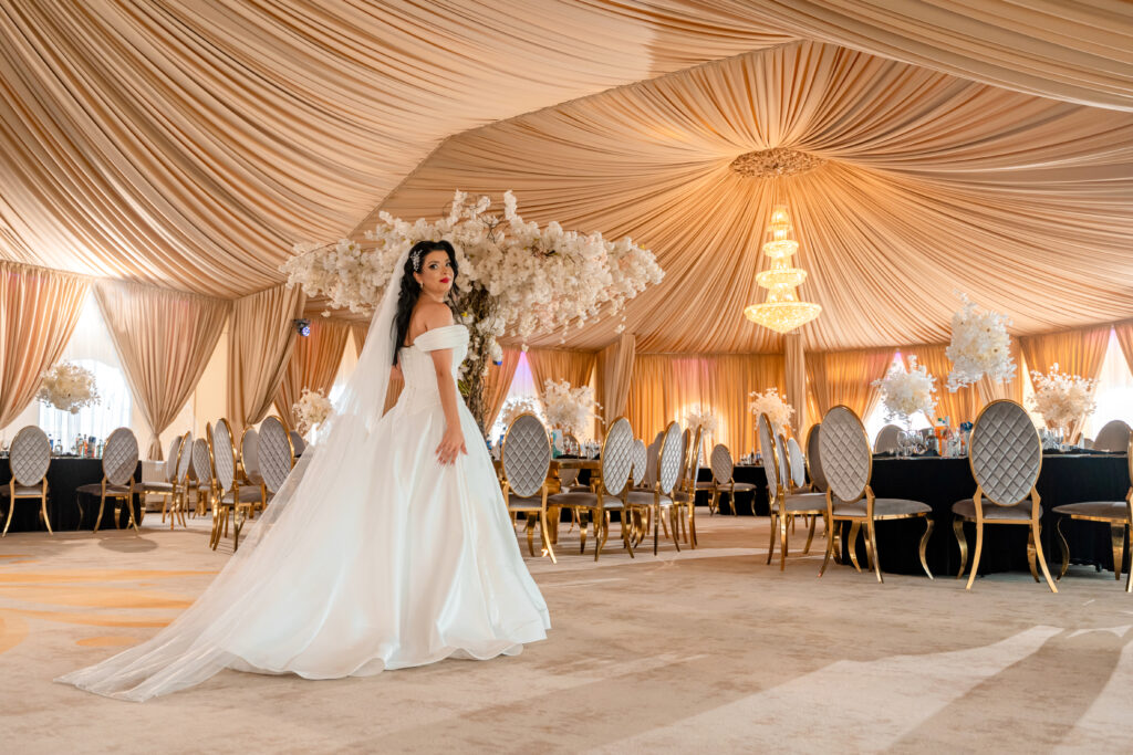 Mireasă într-o sală de evenimente elegant decorată, surprinsă într-un cadru larg cu lumină caldă și detalii rafinate