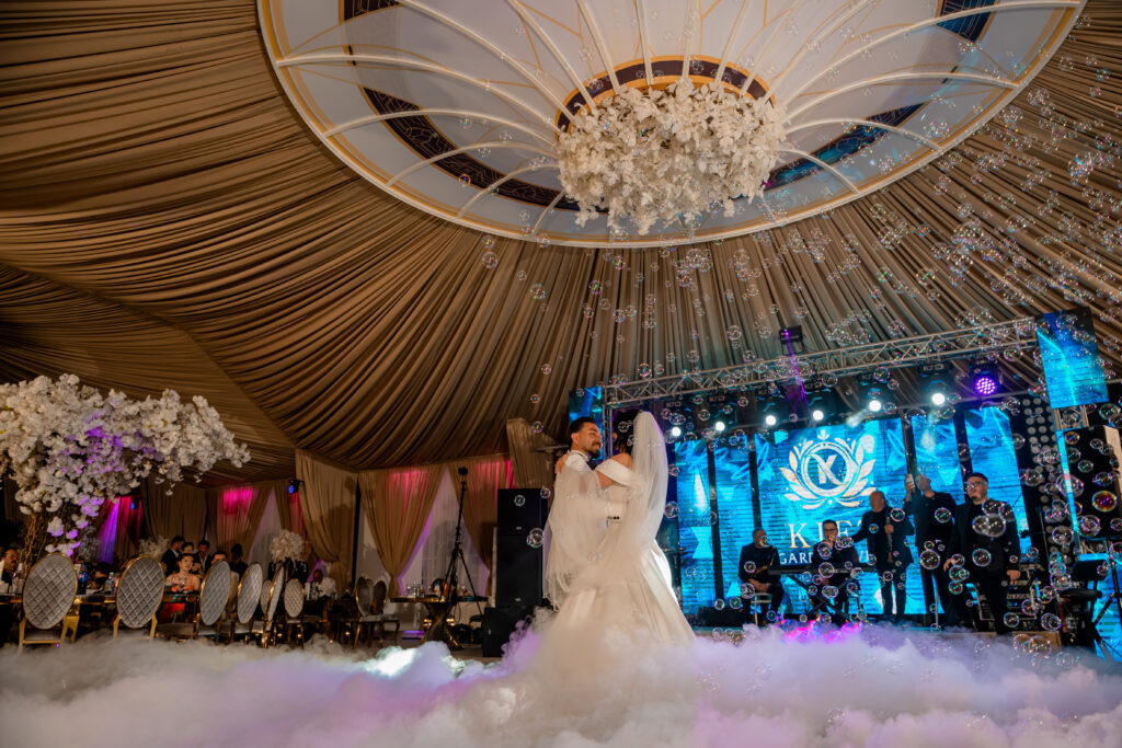 Dansul mirilor pe ring, cu efecte de lumină, fum și baloane de săpun, într-o sală de evenimente elegantă