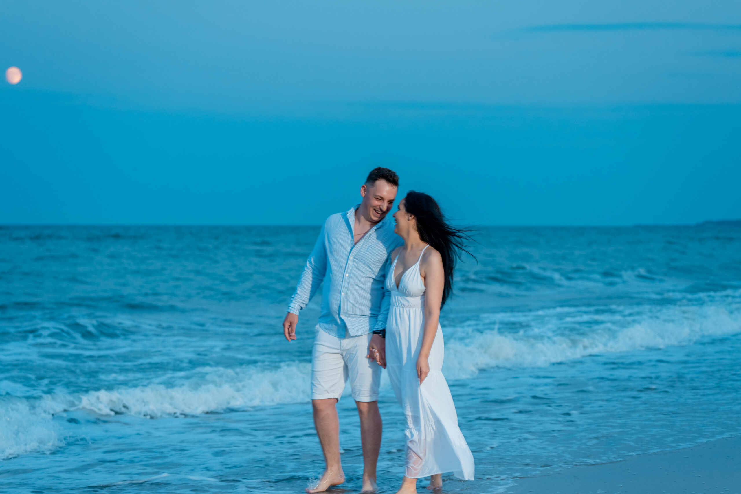 Cuplu plimbându-se pe plajă la apus, într-o ședință foto relaxată pe litoral